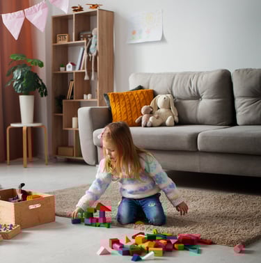 A young girl playing with blocks on the floor and a few toys decorated in background