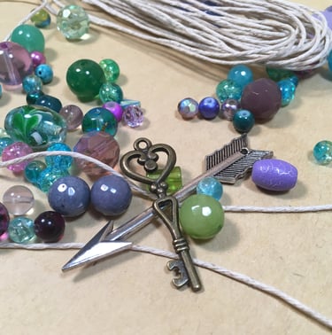 blue, purple, and green beads with key and arrow charm and hemp cord on table