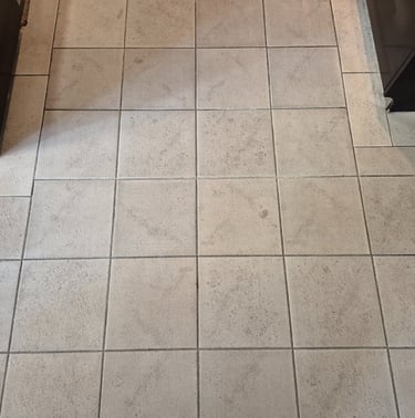 Light grey square ceramic floor tiles with dark grout installed in a kitchen area.