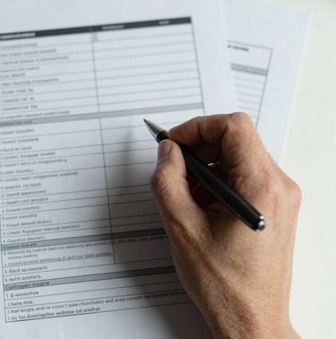 Extreme close-up overhead view of annotated credit analysis documents spread on a clean desk, a hand holding a pen mid-notation, north-facing daylight casting honest flat light across the papers, no faces visible