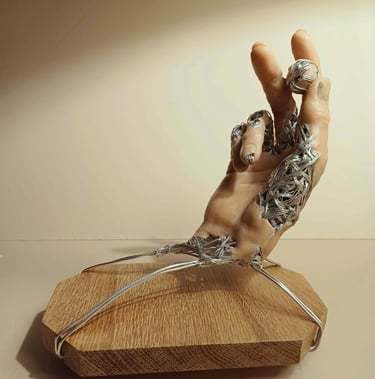 A sculpture of a single hand, part wire, part flesh coloured clay holding a small wire and clay ball