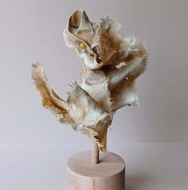 Rear view, showing a clay and canvas sculpture of a female torso, with windswept, ragged clothes.