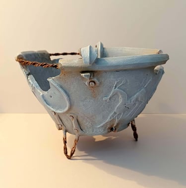 A fragmented, round bowl-like sculpture adorned with symbols and letters, finished in blue-grey hues