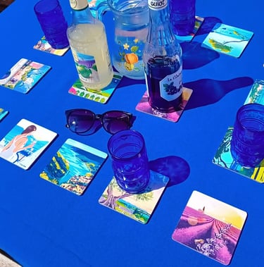 Dessous de verres paysages de Provence Realisart sur une nappe bleue.
