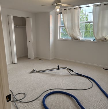 Professional carpet cleaning in an empty bedroom using a steam extraction wand and vacuum hose.