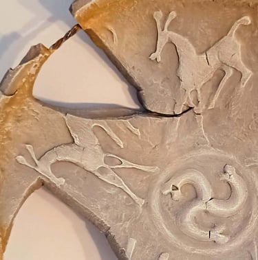 Close up of a bowl-like sculpture with embossed horse figures and symbols in rust/brown hues