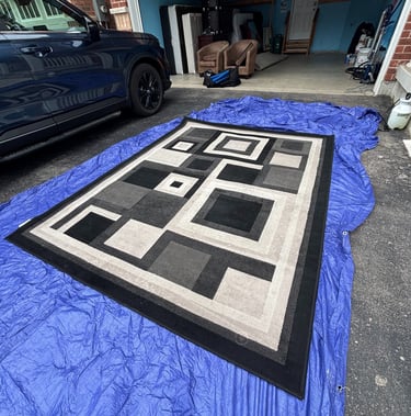 Black and white rug being professionally cleaned on an external work area.