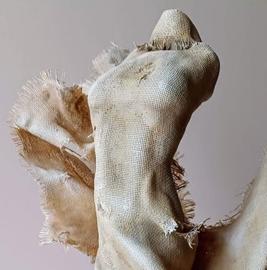 Close up image showing a clay and canvas sculpture of a female torso with windswept, ragged clothes.