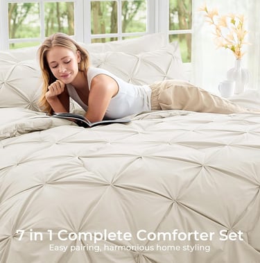 Woman relaxing on a beige pinch pleat comforter set while reading a book in a bright bedroom.