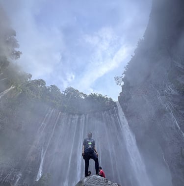 a man standing on a rock in front of a waterfall