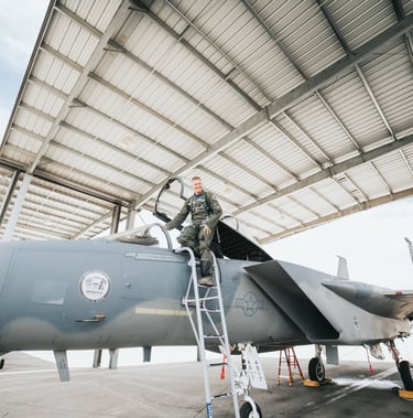 a man in a military uniform standing on a ladder of a fighter jet
