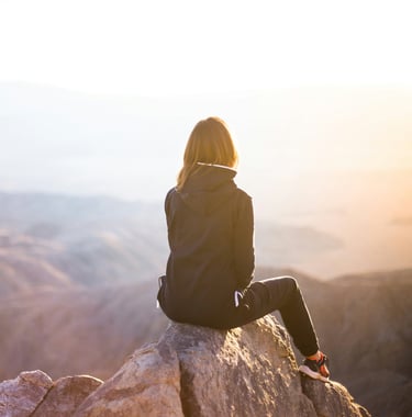 Solo traveler seated on a mountaintop, gazing at a serene sunset view.