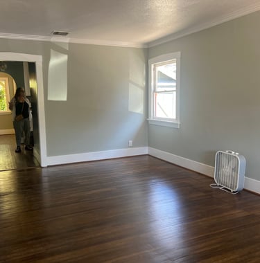 before staging: a person standing in a vacant room with a fan and a fan