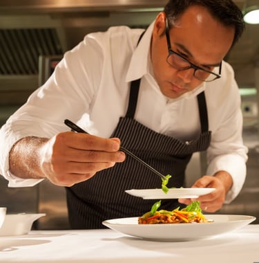Um chef de cozinha finalizando um prato com delicadeza