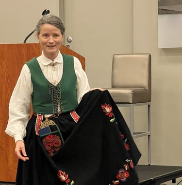 A woman in a bunad with a green vest holding the apron to show detail