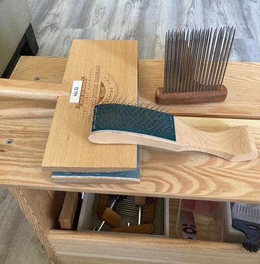 Fiber prep tools on a wood bench.  Includes carders and a comb
