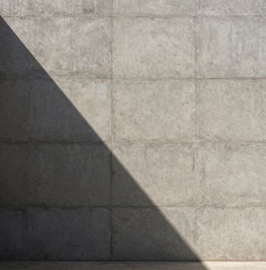 A striking architectural photograph of a minimalist concrete facade in the Middle Eastern / Gulf region. The sun creates a sharp, diagonal shadow across the surface, highlighting the rich textures. Minimal, expensive, and modern.