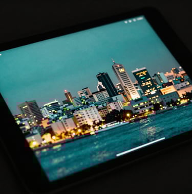 An artistic shot of a digital tablet reflecting the city lights of Algiers at night, showing a blurred professional application screen. High contrast, sea green and black color palette.