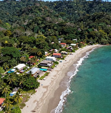 A scenic aerial view of a beachfront development site in Playa Avellanas, Costa Rica, surrounded by lush tropical nature and turquoise waters, professional real estate drone photography.