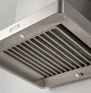 Macro photography detail of a Heisis inertial filter system in a stainless steel range hood. The geometric precision of the metal slats is showcased with sharp, technical lighting and professional minimalist composition.