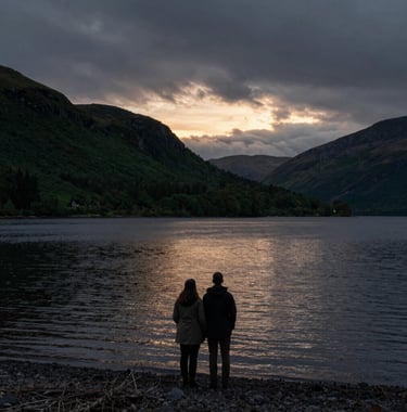 A dark, moody photograph of the silhouette of a couple against a sunset over a calm Scottish loch, with colors ranging from deep forest green to dark slate.