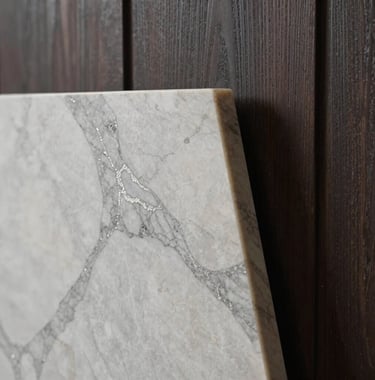 Macro photograph of a luxury interior finish: a slab of premium marble with silver sage veining against a backdrop of deep charcoal wood paneling. The lighting is focused and warm, emphasizing texture.