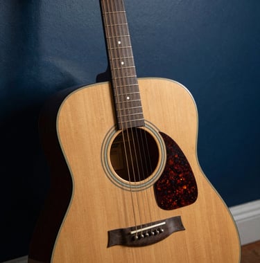 A detailed close-up of a weathered acoustic guitar leaning against a dark blue studio wall, featuring soft shadows and golden hour lighting, North American coastal aesthetic.