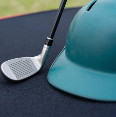 Close-up of high-tech sports equipment including a sleek white golf club and a matte teal baseball helmet resting on a dark navy surface. Soft natural light highlights the premium textures.
