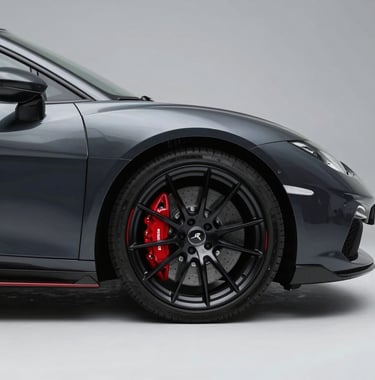 A side profile shot of a luxury sports car's alloy wheel and red brake caliper. The car is finished in a Deep Obsidian paint that reflects the soft ambient studio lighting. The background is a clean Misty Slate grey.