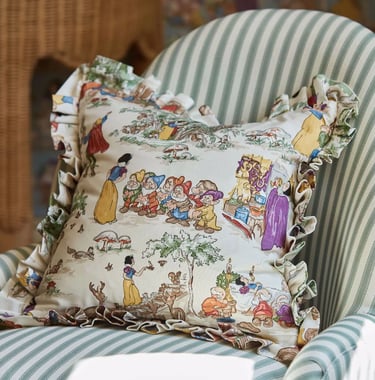 Un coussin aux motifs des sept nains et blanche neige, posé sur un fauteuil à rayures