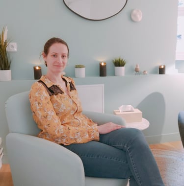 Une hypnothérapeute assise sur un fauteuil dans un cabinet d'hypnothérapie et un miroir sur le mur