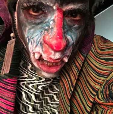 David Noir • une créature au visage coloré comme celui d'un mandrill portant des vêtements arty