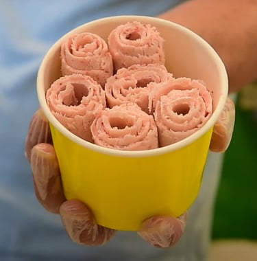 Hand holding a yellow cup of fresh strawberry rolled ice cream swirls.