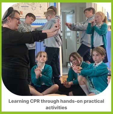 A first Aid instructor sat amongst a group of children showing them hand placement for CPR