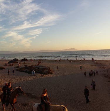 a couple of people riding horses on a beach