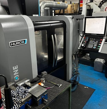 Industrial Hurco CNC machine center in a manufacturing workshop with precision metal parts and control panel.