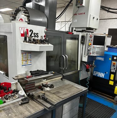 Haas VF-2ss vertical machining center and VMC 1200 K industrial CNC milling machine in a workshop.