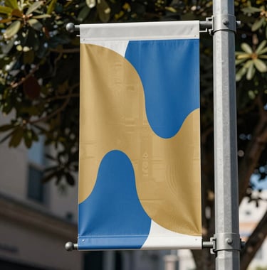 A close-up of a stylish street banner in West Hollywood displaying abstract creative designs in gold and medium blue, with soft sunlight filtering through nearby trees.
