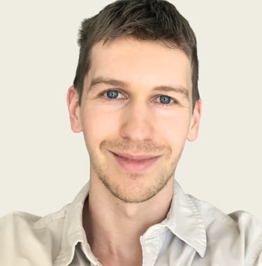 Professional headshot of a smiling man with short brown hair and blue eyes wearing a beige button-down shirt.