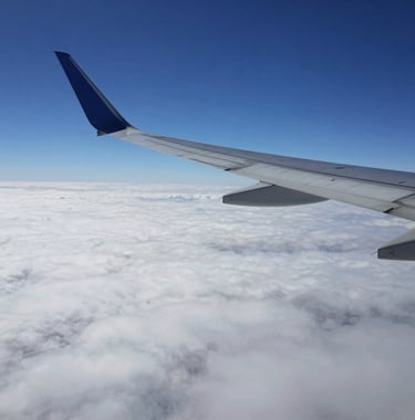 A wide shot of a modern airplane wing cutting through a sea of white clouds against a deep dark blue sky. Professional aerial photography, clean and inspiring a sense of freedom and ease.