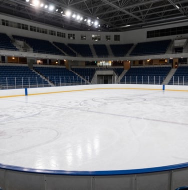 Photography of a modern collegiate ice rink in a North American / US Southern university city, wide angle showing clean white ice and blue stadium seating, professional lighting.