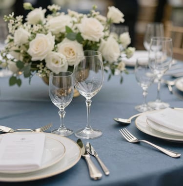 Extreme close-up of a high-end corporate gala dinner table setting, crystal glassware, silver cutlery, elegant slate blue linens, white floral centerpieces, Parisian elegance, European / French.