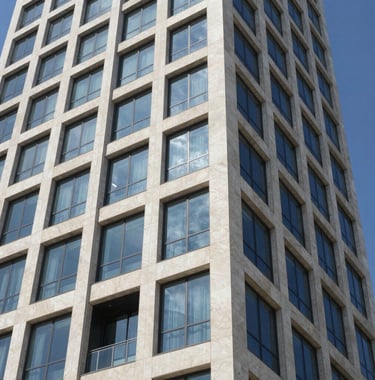 Close-up architectural shot of a modern glass and white stone facade of a luxury residential tower in the Ir Yamim district, Netanya. Clear blue sky reflected in the windows. Sophisticated and high-tech.