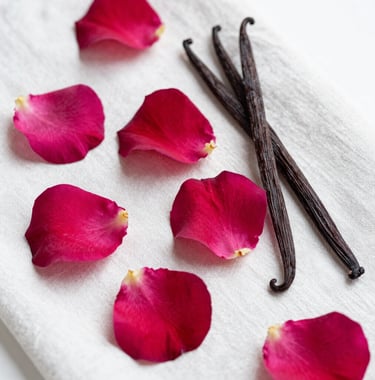Fine art photography of fresh rose petals and vanilla beans on a white linen cloth, capturing the raw ingredients of a luxury perfume. Soft, natural lighting in a French studio.