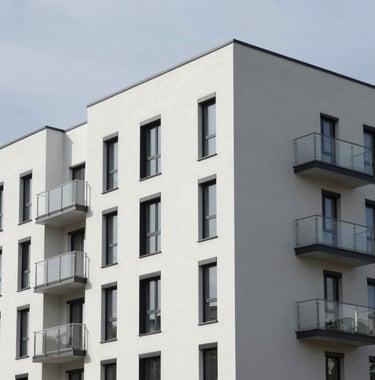 A modern residential building exterior featuring clean lines and a monochromatic palette of whites and greys. Professional architectural photography under a clear Northern European sky.
