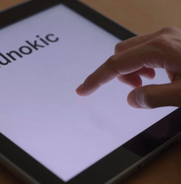A close-up shot of a human hand using a touch screen on a modern piece of digital equipment. The screen reflects soft lavender light and displays clean, modern typography and graphics.