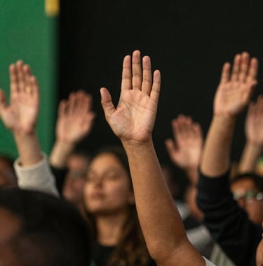 Close up of diverse hands raised in worship, warm stage lighting with gold accents (#D8B863) against a dark premium backdrop. High-end photography style.