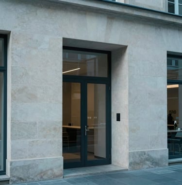 Professional architectural photography of a Luxembourgish boutique office lobby. Soft textures, stone walls in off-white, and a sense of quiet discretion and authority. The palette features slate blue and light gray-blue tones.