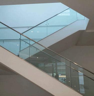 Architectural photography of a modern staircase in a luxury building in Luxembourg. Clean lines, glass railings, and a minimalist aesthetic. The image uses a palette of light blue and off white, conveying a sense of transparency and order.