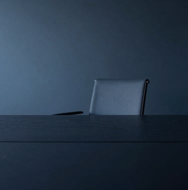 An abstract photography of a minimalist boardroom in Luxembourg with a single, elegant chair and a large dark table. The lighting is dramatic but soft, highlighting the textures of high-quality materials. Palette: dark navy and slate blue.